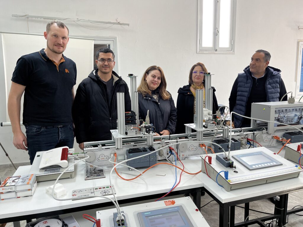 5 Personen stehen vor einer Industrie-4.0-Trainingsanlage