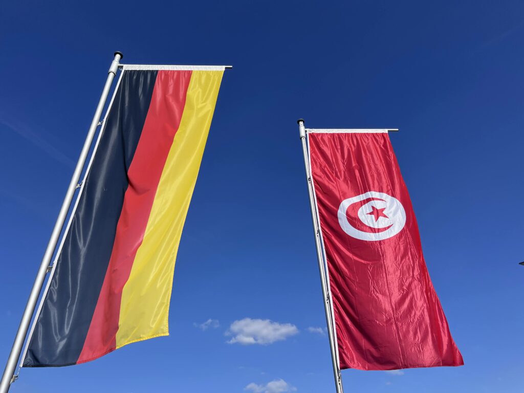 Die Flaggen von Deutschland und Tunesien, im Hintergrund blauer Himmel